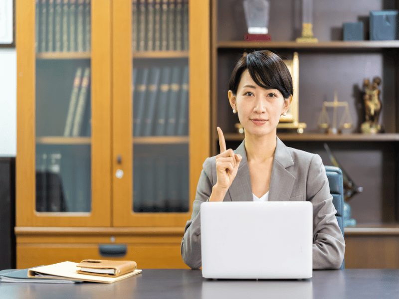 事務所で人差し指を立てて凛と座る女性行政書士の写真